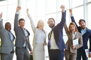 Group of ecstatic business partners looking at camera with raised arms