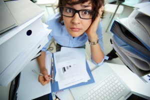 Perplexed accountant doing financial reports surrounded by huge piles of documents