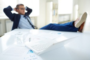 Image of laptop at workplace and businessman relaxing in office