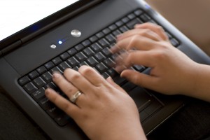 Detail of a woman typing rapidly on a laptop keyboard.