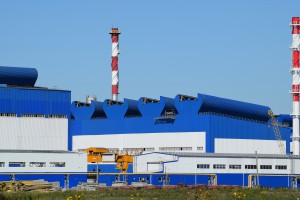 Big plant for processing scrap metal. Huge factory old metal refiner. Blue roof of the factory building. Exhaust pipes, radiators, cooling industrial units as well as office buildings.